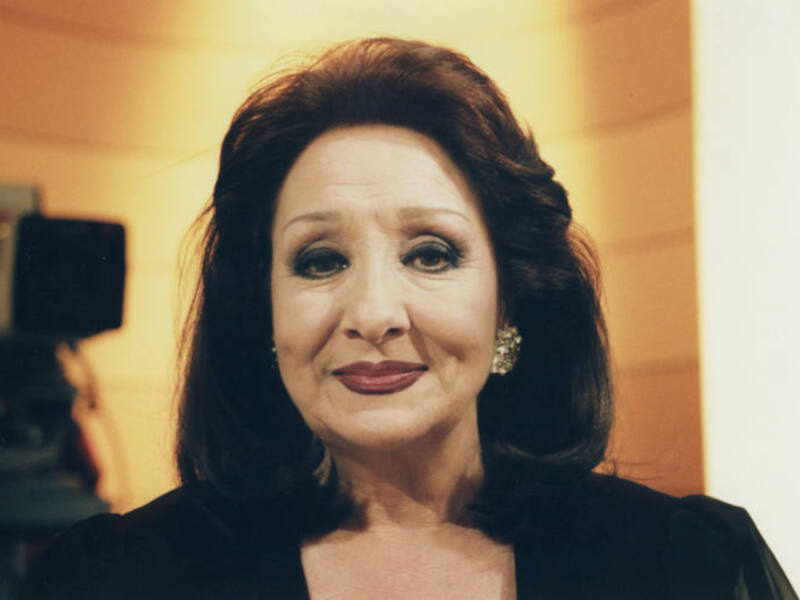Elegante mujer con maquillaje suave y cabello ondulado, posando con elegancia en un ambiente interior con iluminación cálida.