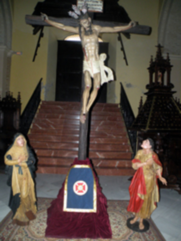 Representación del Cristo crucificado en un interior de iglesia, rodeado por figuras de la Virgen y San Juan.