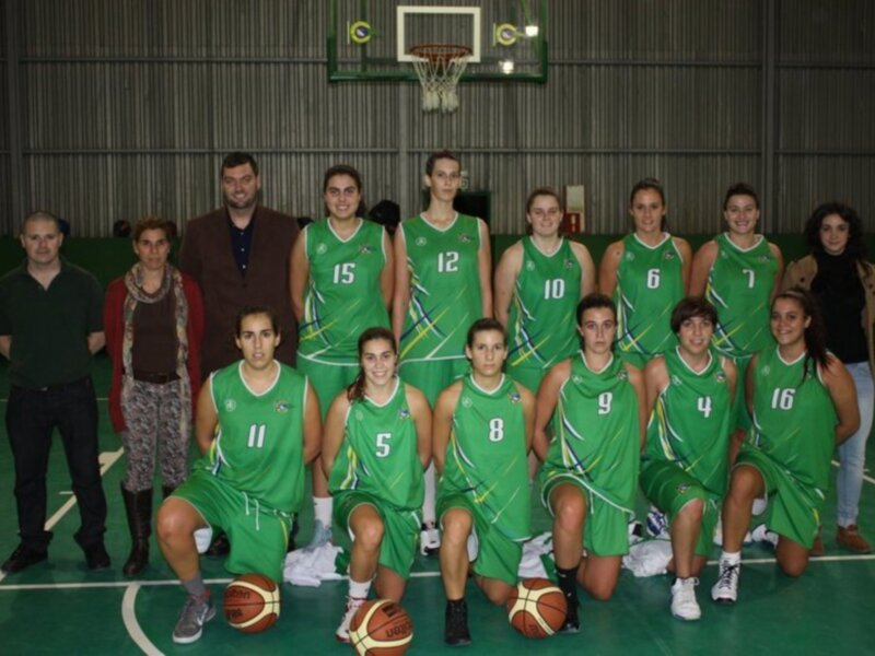 Equipo de baloncesto femenino en uniforme verde posando en una cancha de baloncesto.