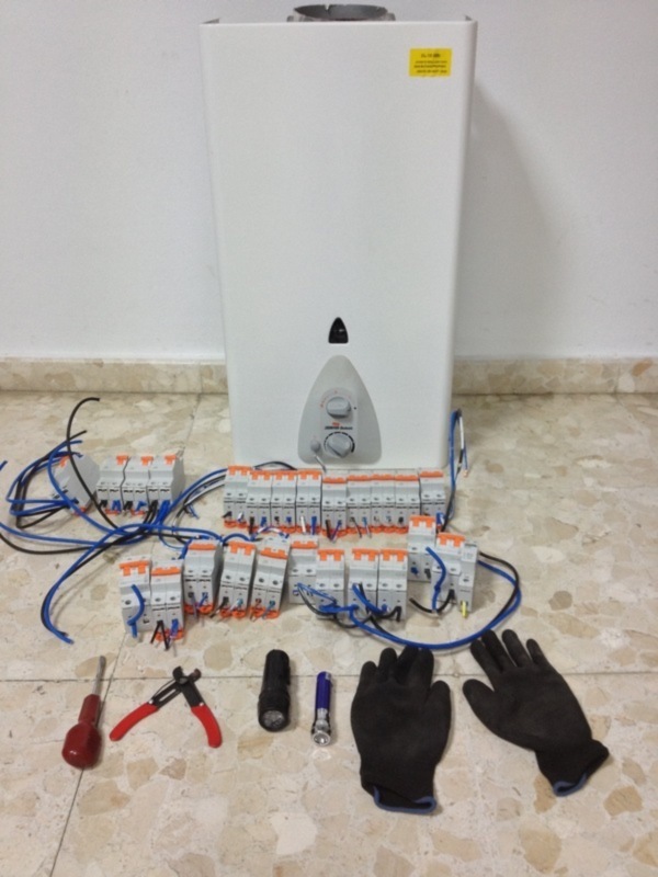 Instalación eléctrica con interruptores, cables y herramientas alrededor de un calentador de agua.
