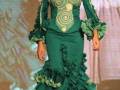 Modela en el desfile de moda con un vestido de flamenca verde con detalles bordados y volantes en la falda.