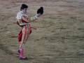 Un torero en una plaza de toros, realizando una faena con un capote y un chaleco tradicional, en una arena de arena.
