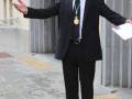 Un hombre en traje negro con una medalla colgada, posando con las manos extendidas hacia el aire.