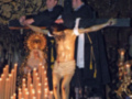 Imagen religiosa con un crucificado y una imagen de la Virgen en el fondo, rodeados por velas encendidas.