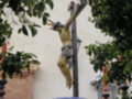 Escultura de Jesús crucificado en una cruz, rodeado por flores azules y árboles.