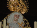 Imagen de una Virgen con un halo dorado y una capa blanca, rodeada por velas.