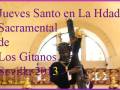 Un hombre vestido con trajes tradicionales sostiene una cruz en la imagen. La frase "Jueves Santo en La Hdad. Sacramental de Los Gitanos Sevilla 2013" se encuentra en la parte superior. La foto es de DonaldPress y muestra una escena religiosa con un fondo dorado en el cielo.