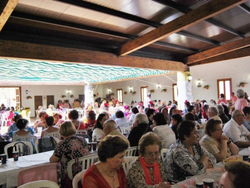 Fiesta comunitaria con personas mayores disfrutando de una reunión en un salón decorado con mantas y flores.