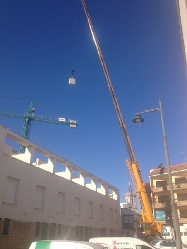 Trabajos de construcción con grúa levantando materiales en un edificio en proceso.