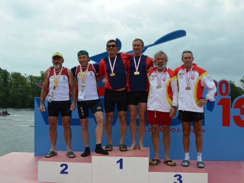 Campeones del evento de remo en el podio con medallas y palas de remo en el fondo.