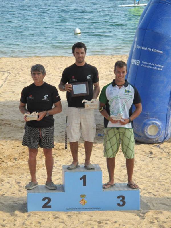 Tres participantes en un podio en la playa, posando con sus trofeos. El centro es el ganador, el lado izquierdo el segundo y el derecho el tercero.