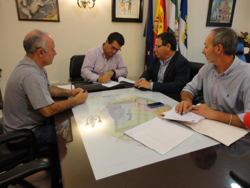 Cuatro personas en una reunión, uno de ellos firma un documento mientras los otros observan.