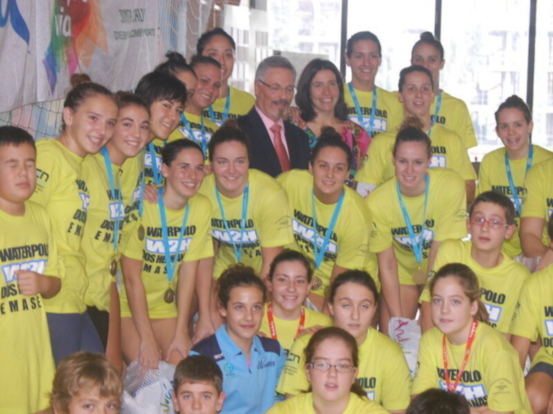 Equipo de waterpolo con medallas y camisetas amarillas celebrando juntos.