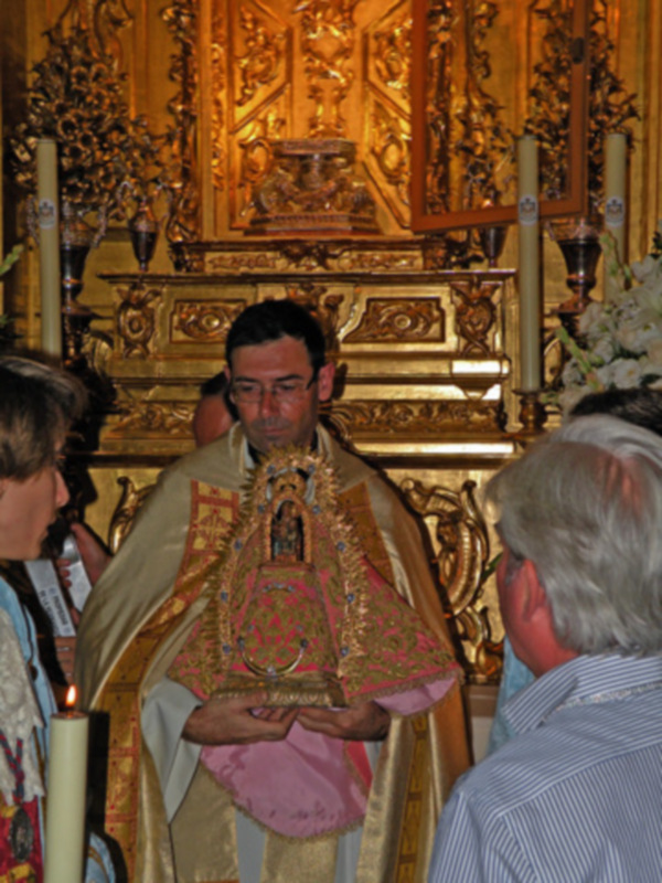 Un sacerdote sostiene una imagen religiosa durante una ceremonia en un templo ornamental con adornos dorados.