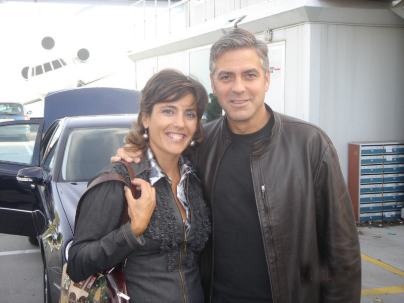 Una pareja sonríe frente a un vehículo y un avión en el fondo.
