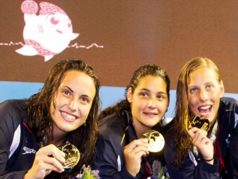 Tres nadadoras celebran en el podio con medallas de oro.