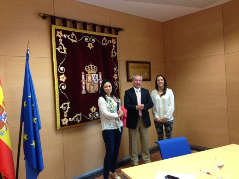Tres personas posando en una sala con una bandera española y una bandera europea en el fondo.