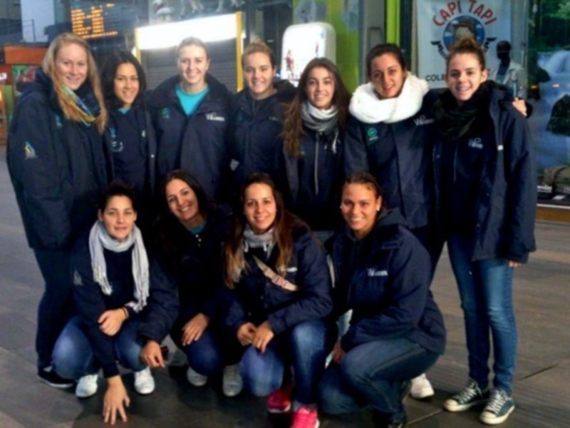 Una foto de un grupo de mujeres en trajes de trabajo, posando en una calle con edificios y carteles en el fondo.
