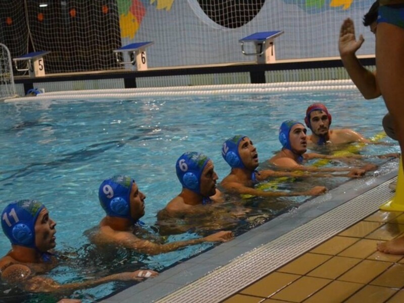 Equipo de waterpolo en una charla técnica antes del entrenamiento en una piscina cubierta.