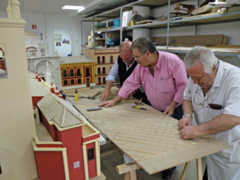 Tres hombres trabajan en la construcción de modelos arquitectónicos en un taller bien organizado.