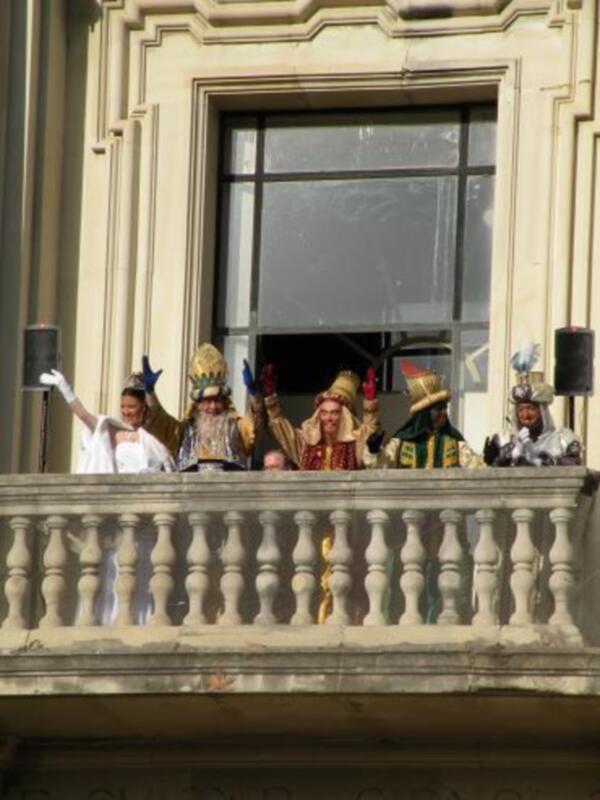 Personas con disfraces y sombreros en un balcón de un edificio histórico. La escena sugiere una celebración o evento festivo. La estructura del edificio y la postura de las personas sugieren una atmósfera festiva y festiva.