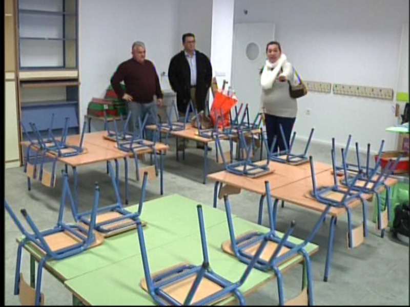 Personas visitando una sala de aula vacía con mesas y sillas desordenadas.