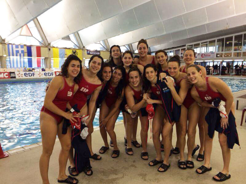 Equipo femenino de natación posando en la piscina, con banderas de países en el fondo.