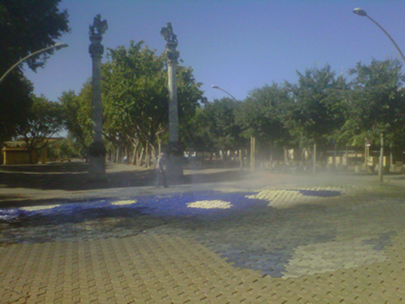 Un parque con dos columnas de piedra y un monumento en el centro, rodeado de árboles y una fuente de agua.