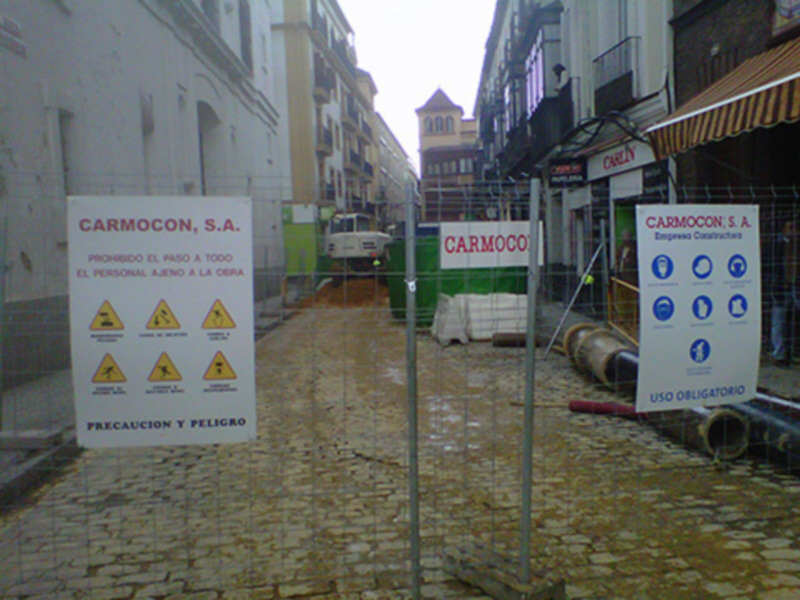 Zona de construcción con carteles informativos y advertencias de seguridad en una calle urbana.