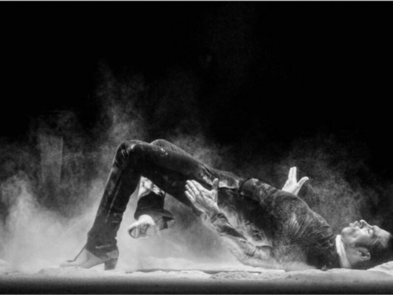 Danza en blanco y negro con polvo en movimiento, capturando la gracia y la fuerza del movimiento.