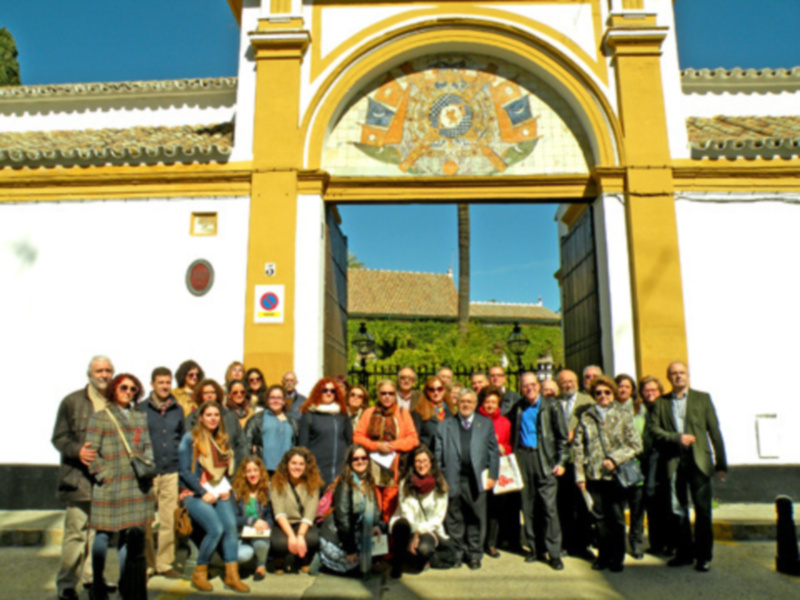 Una reunión de profesionales en un entorno histórico, posiblemente en un museo o palacio, con personas vestidas formalmente y una arquitectura de estilo clásico en el fondo.