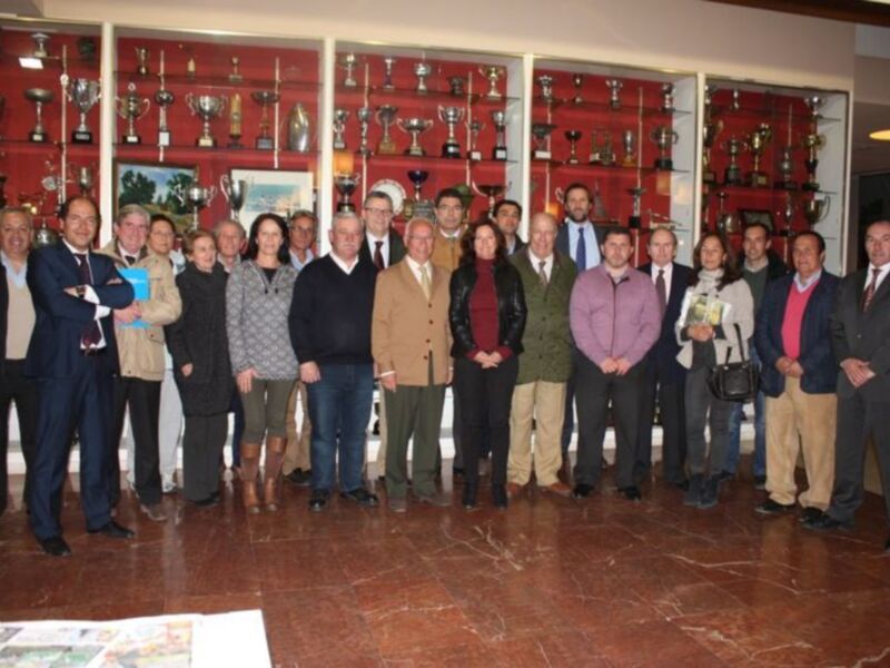 Una reunión de trabajo en un salón con estanterías de trofeos en el fondo.