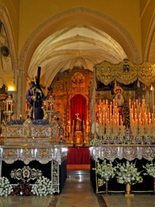 Interior de una iglesia con altar ornado, altares laterales y candelabros de luz.