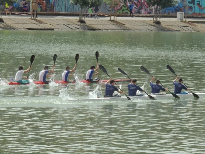 Un grupo de personas kayacando en un lago, con árboles y grafitis en el fondo.