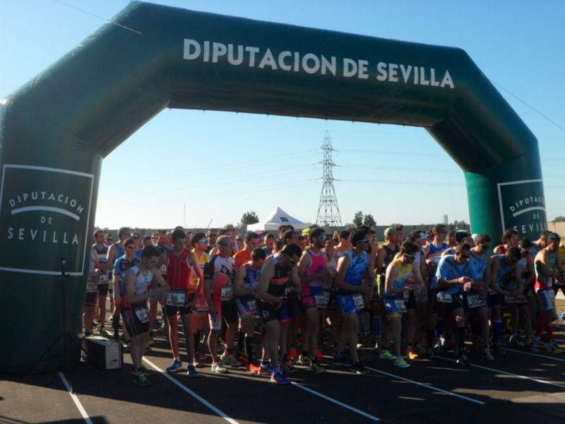 Atleta esperando en la línea de salida de una carrera de triatlón bajo el arco de la Diputación de Sevilla.