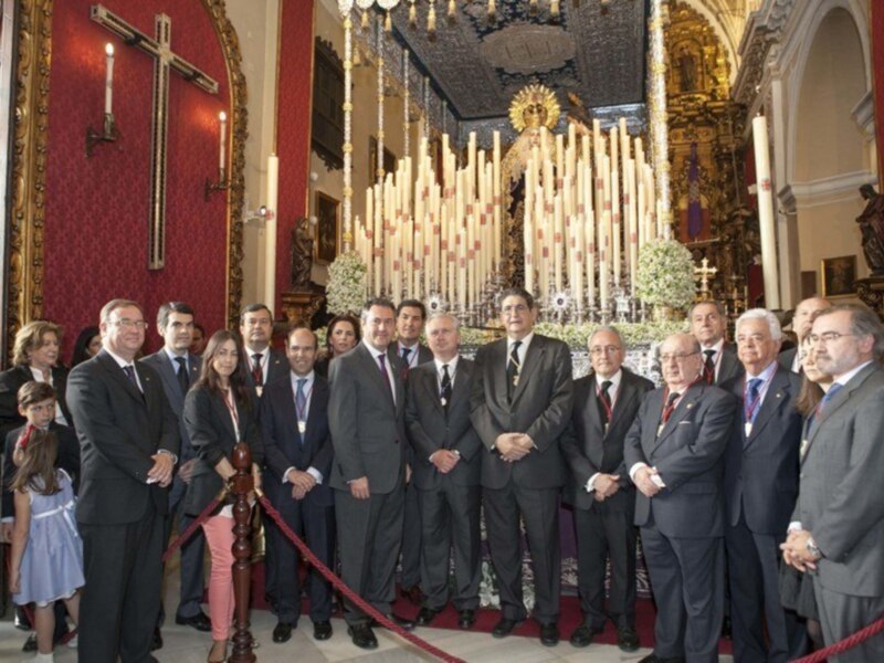 Gruppo di persone in abiti formali posano per una foto all'interno di una chiesa ornata con candele e statue.