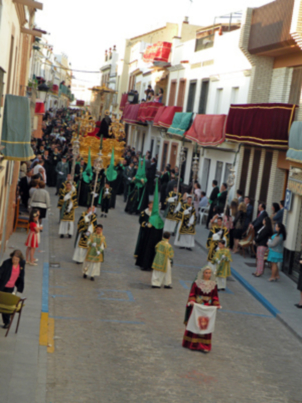 Procesión religiosa con vestimentas tradicionales y estandartes en una calle de pueblo.