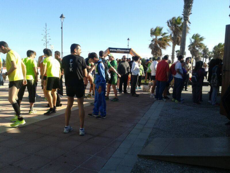 Atletas se preparan para una carrera en una plaza con palmeras y un cartel de la carrera en el fondo.