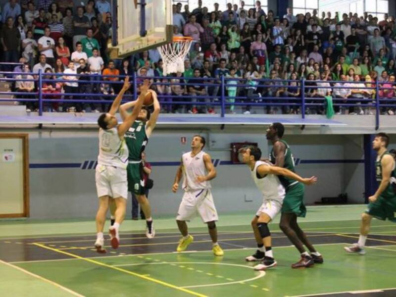 Jugadores en acción durante un partido de baloncesto en una cancha con público en las gradas.