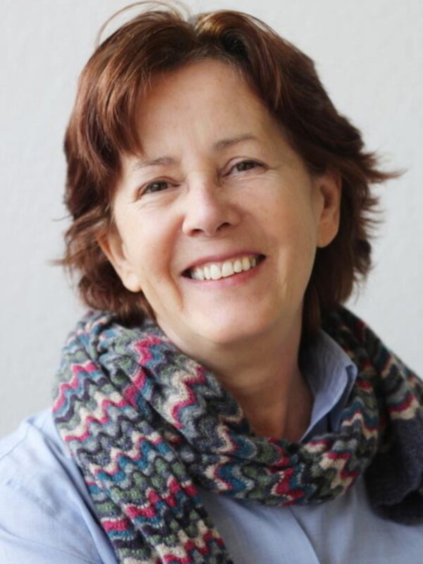 Una mujer con cabello corto y rojo, sonriendo y llevando una bufanda tejida con tonos de azul, rosa y beige.