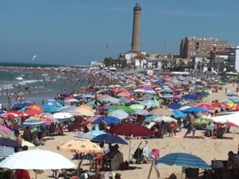 Playa con muchas personas bajo sombrillas y una torre en el fondo.