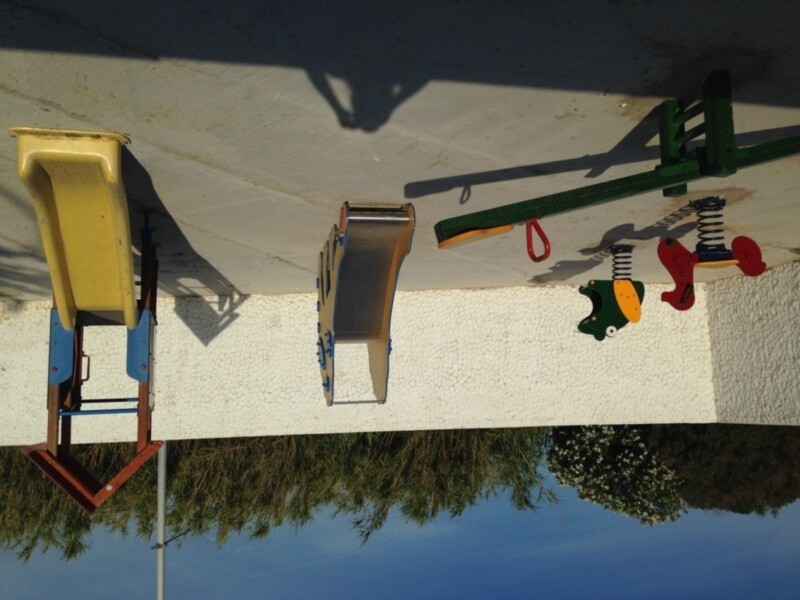 Juguete de construcción en un parque infantil con sombra de un árbol en el fondo.