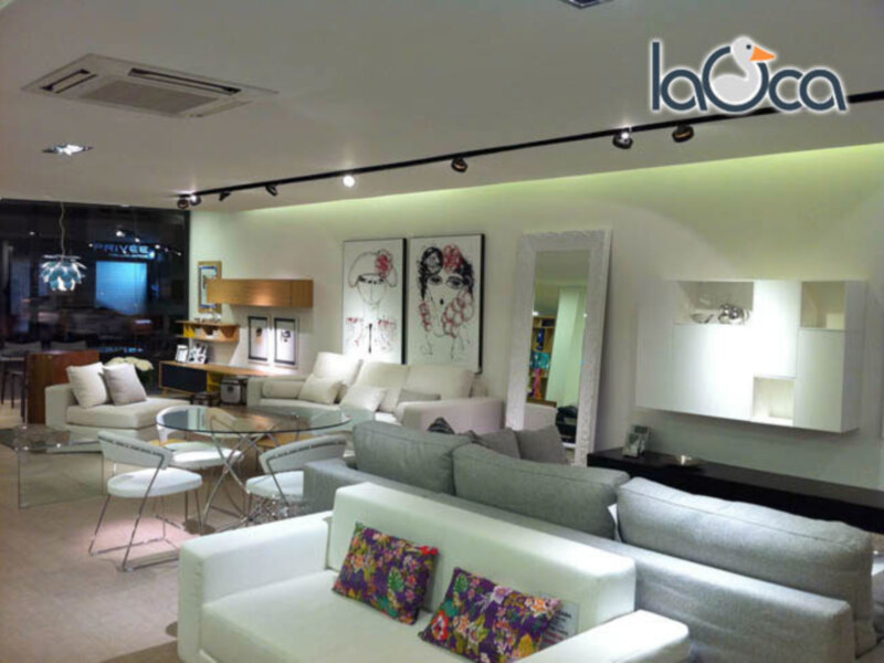Elegante sala de estar con sofás blancos, mesas de cristal, lámparas modernas y una televisión en la pared. El diseño minimalista combina sofisticación y comodidad.