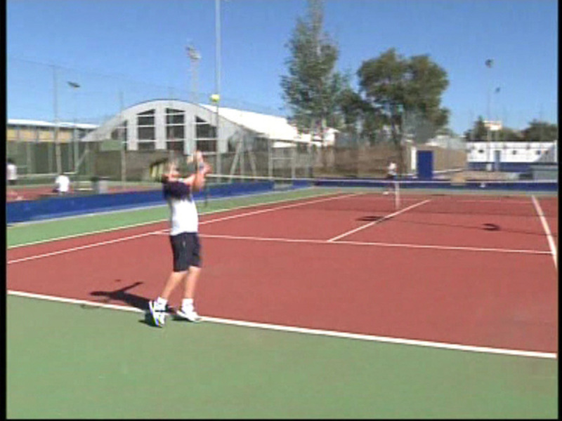 Un tenista en acción, preparándose para un golpe en un campo de tenis con una pista roja y verde, mientras el cielo es azul claro y hay árboles en el fondo.