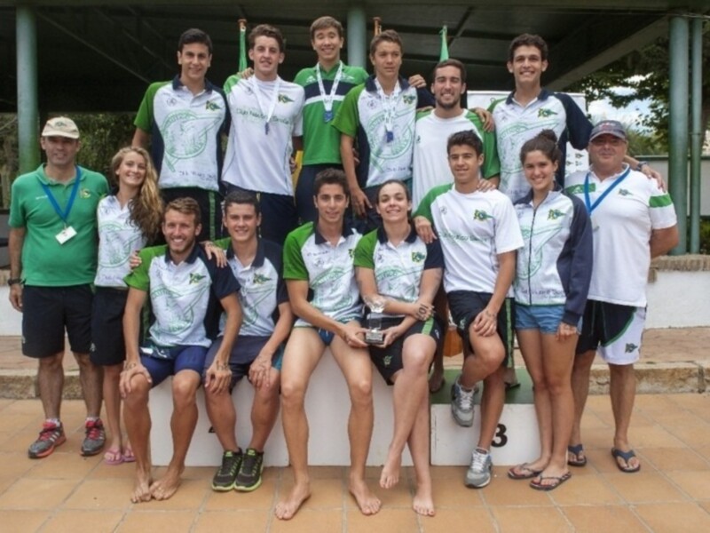 Equipo de natación celebrando una victoria, con medallas y sonrisas en el podio.