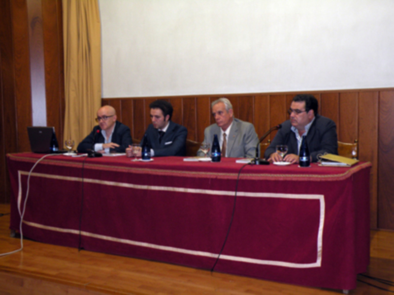 Reunión de expertos en una sala con mesa rectangular y sillas, cubierta con tela roja y dorada, en un ambiente formal.