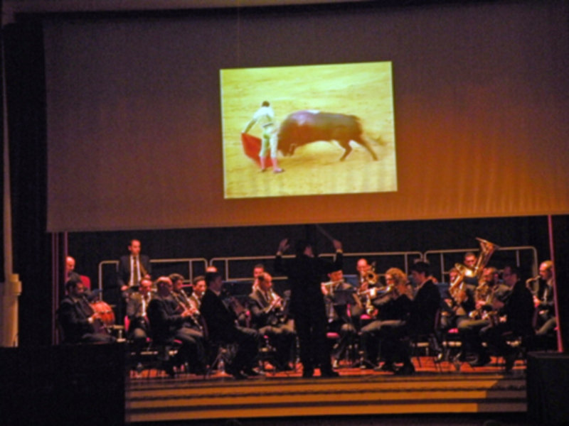 Orquesta en escenario con proyección de una escena de toros en pantalla detrás.