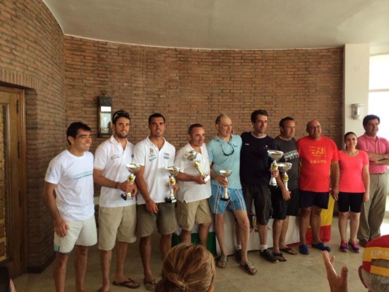 Equipo ganador de una competición deportiva celebrada en un local con pared de ladrillo y trofeos en mano.