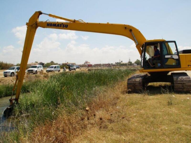 Excavadora de construcción de marca Komatsu en un campo despejado, con vehículos de trabajo en el fondo.