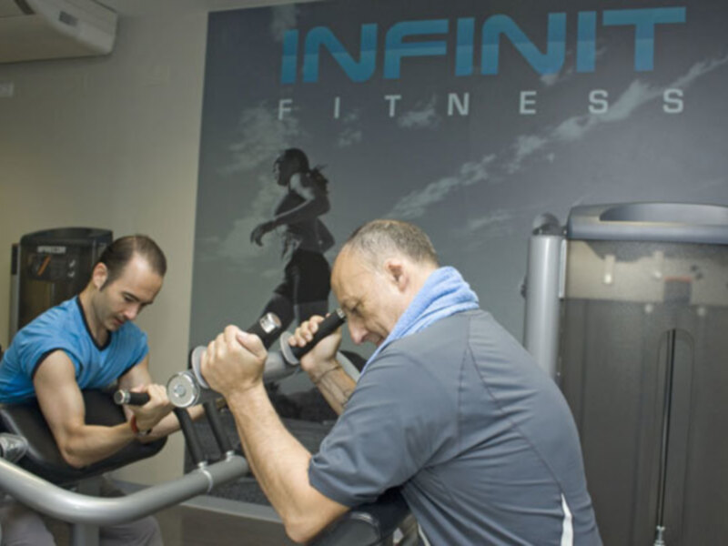 Un hombre se ejercita en una máquina de fitness mientras un instructor le da instrucciones.